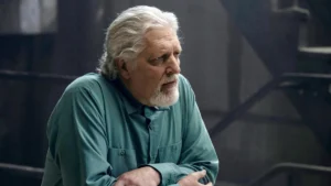 Clancy Brown plays Sal Maroni, an elderly man with a stern gaze and white beard, dressed in teal.